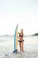 portrait de souriant Jeune femme permanent avec planche de surf à le plage photo