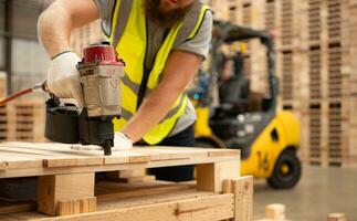 Jeune ouvriers travail dans une travail du bois usine, en utilisant une cloutage machine à assembler en bois palettes photo