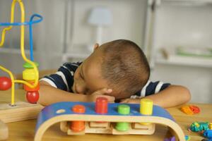 garçon en train de dormir sur le table à l'intérieur le maison après en jouant avec jouets. photo