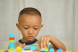 asiatique garçon en jouant avec éducatif jouets là sont beaucoup magnifique couleurs sur le table dans le maison. photo