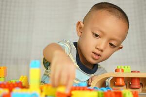 asiatique garçon en jouant avec éducatif jouets là sont beaucoup magnifique couleurs sur le table dans le maison. photo