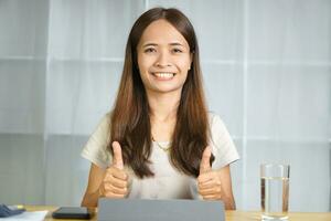 asiatique femme travail à Accueil élever votre main comme excellent photo