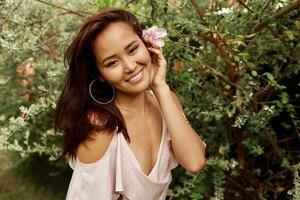 gracieux asiatique femme avec parfait peau et hibiscus fleur dans Cheveux posant plus de bois mur et tropical les plantes. été mode portrait. photo