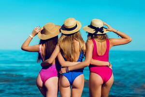 sexy dos de Trois magnifique femmes avec parfait corps sur tropical plage dans petit élégant bikini. photo