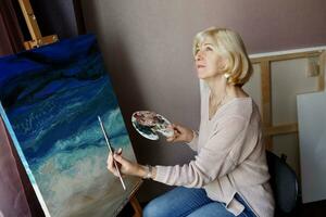 intérieur mode de vie portrait de mature femme dessine avec acrylique sur toile. rester à maison. photo