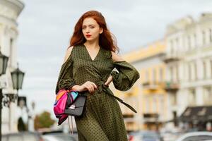 plein longueur image de élégant gingembre femme dans vert robe en marchant dans Paris. à la mode modèle avec rouge lèvres et incroyable ondulé Cheveux. photo