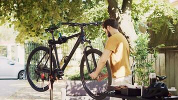 déterminé Masculin cycliste soigneusement enlever endommagé vélo pneu pour remplacer avec nouveau. Jeune caucasien homme relâchement et porter bicyclette roue pour plus loin entretien dans Accueil cour. photo