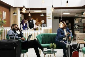 fatigué gens avec bagage attendez à Hôtel lobby, africain américain homme et femme touristes attendez à enregistrement. noir famille couple arrivée à recours pour vacances, repos après longue vol photo