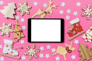 vue de dessus de la tablette numérique, fond rose décoré de jouets festifs et de symboles de noël rennes et arbres du nouvel an. notion de vacances photo