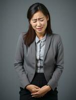 asiatique femme apparaît à être dans douleur sur gris Contexte ai génératif photo