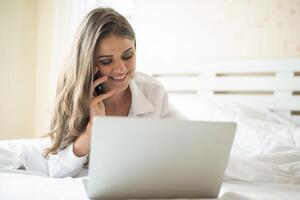 heureuse belle femme travaillant sur un ordinateur portable sur le lit dans la maison photo