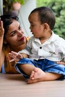 aimant maman porter de sa bébé à Accueil balcon. brillant portrait de content maman en portant enfant dans sa mains. mère avec sa peu 1 année vieux fils. photo