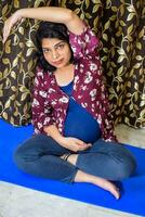 Enceinte femme Faire grossesse yoga pose confortable à Accueil avec ventre, Enceinte femme pratiquant Facile yoga pas à maison, grossesse yoga et aptitude pose photo