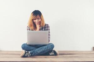 jeune femme hipster assise sur un plancher en bois avec les jambes croisées. photo