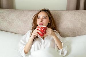 portrait belle femme asiatique se réveiller et tenant une tasse de café ou une tasse sur le lit le matin