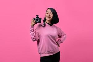 Happy smiling young woman holding camera sur fond rose photo