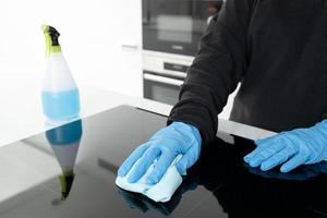 mains dans un gant de protection nettoyant une cuisinière électrique moderne avec un chiffon photo