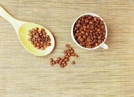 grains de café torréfiés dans une tasse blanche avec une cuillère en bois photo