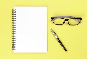 cahier, stylo et lunettes sur fond jaune photo
