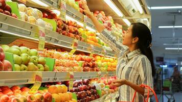 portrait de une magnifique asiatique ou indonésien femme achat fruit arrangé sur fruit grille dans une supermarché photo