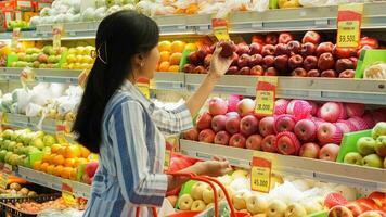 portrait de une magnifique asiatique ou indonésien femme achat fruit arrangé sur fruit grille dans une supermarché photo