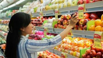 portrait de une magnifique asiatique ou indonésien femme achat fruit arrangé sur fruit grille dans une supermarché photo