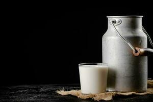 rustique Lait dans une pouvez et une verre sur le tableau. photo