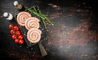 brut saucisses sur une Coupe planche avec une brin de Romarin et tomates. photo