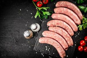 brut saucisses sur une pierre planche avec épices, tomates et herbes. photo