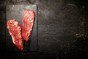 brut steak sur une pierre planche. sur une noir Contexte. photo