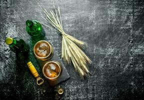 Bière dans des lunettes et bouteilles avec une bouquet de épillets. photo