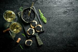 des sandwichs avec noir caviar, caviar dans une bol et blanc du vin. photo