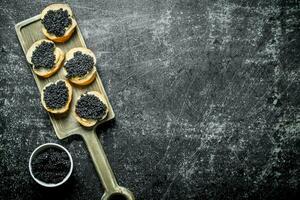 des sandwichs avec noir caviar sur une Coupe planche et caviar dans une bol. photo