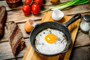 frit Oeuf dans une la poêle avec pain, tomates et vert oignons. photo