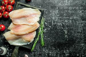 poisson filet sur une Coupe planche avec tomates, Romarin et sel. photo