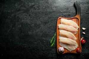 poisson filet sur une Coupe planche avec Romarin, Ail et tomates. photo