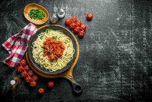 Pâtes spaghetti avec bolognaise sauce dans la poêle avec tomates, serviette et haché légumes verts dans bol. photo