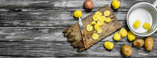 tranché patates sur une Coupe planche avec une couteau et pelé patates dans une casserole. photo