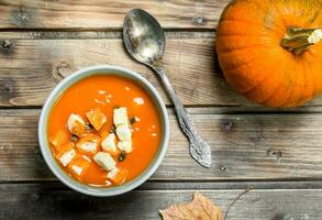 citrouille soupe dans une bol avec une cuillère et une entier citrouille. photo