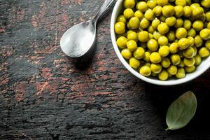 en conserve vert pois dans bol avec cuillère et baie feuille. photo