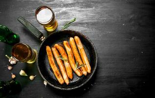 saucisses dans une friture la poêle avec une verre de bière. photo