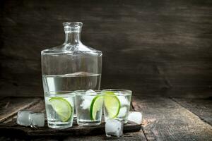 Vodka coups avec citron vert et la glace sur le planche. photo