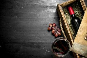 bouteille de rouge du vin dans un vieux boîte avec une branche de les raisins. photo