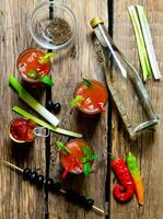 Trois cocktail avec Ingrédients - glace, tomates, vodka, céleri, poivre, Olives et menthe feuilles sur une en bois table . photo