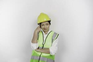 une réfléchi Jeune femme la main d'oeuvre ouvrier portant sécurité casque et gilet est à la recherche de côté à un idée sur copie espace , isolé par blanc Contexte. le travail journée concept. photo