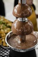 Machine de restauration de fontaine de chocolat avec des brochettes de fruit sur la table rustique de buffet photo
