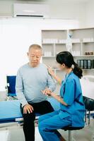 asiatique médecin dans blanc costume prendre Remarques tandis que discuter et asiatique âgé, homme patient qui mensonge sur lit avec recevoir saline Solution dans hôpital ou clinique. photo