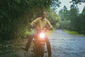 asiatique homme équitation petit enduro moto traversée écoulement ruisseau dans forêt parmi pluie chute photo