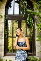 jolie Jeune femme en utilisant mobile téléphone par le vieux maison avec lierre photo