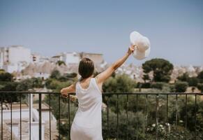 une Jeune femme dans une blanc robe et une chapeau pendant touristique visite dans alborebello, Italie photo